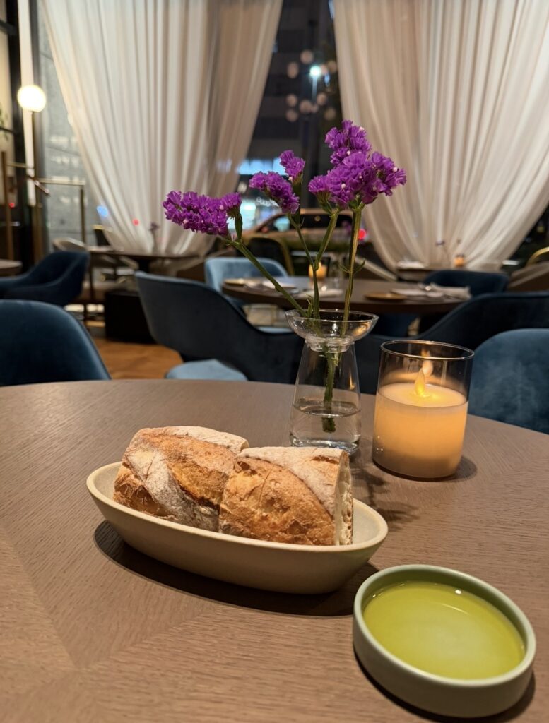 New American Dining GOTTAで提供されるパンとオリーブオイル。テーブルには花とキャンドルが飾られ、Bread & Coffee IKEDAYAMA本店のパンが上質な雰囲気の中で提供されている様子。