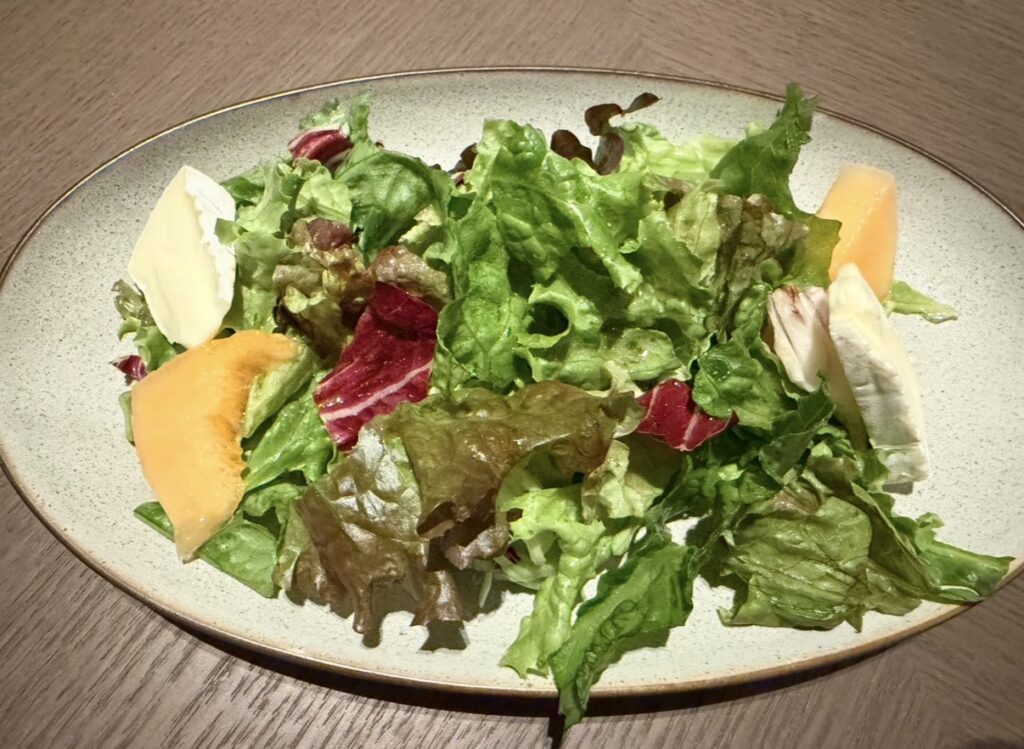 New American Dining GOTTAの「季節のフルーツとブリーチーズのサラダ」。みずみずしいメロンとブリーチーズ、たっぷりのリーフ野菜が盛り付けられた彩りの良いサラダ。