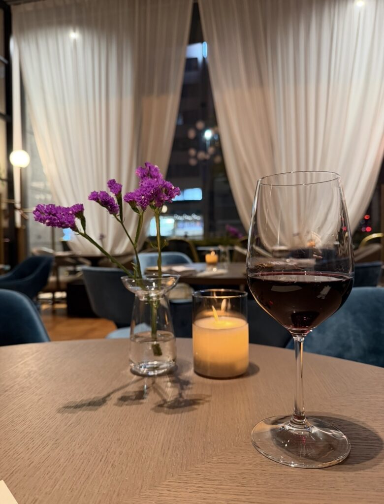 キャンドルが灯る夜の店内で、テーブルに置かれた赤ワインのグラスと花瓶の紫の花。落ち着いた雰囲気の中でフリーフローの赤ワインを楽しんでいる様子が伝わる写真。