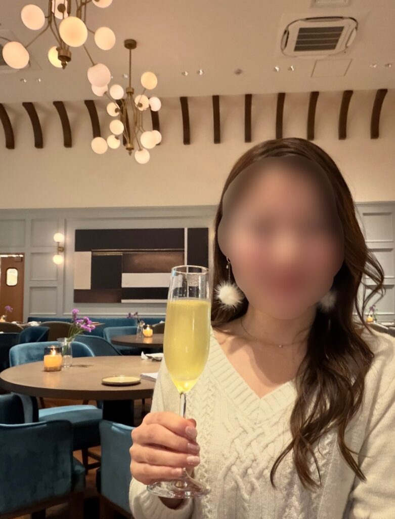 ブログ運営者COCOが、New American Dining GOTTAの店内でスパークリングワインを持って乾杯している様子（※顔はぼかし加工をしています）