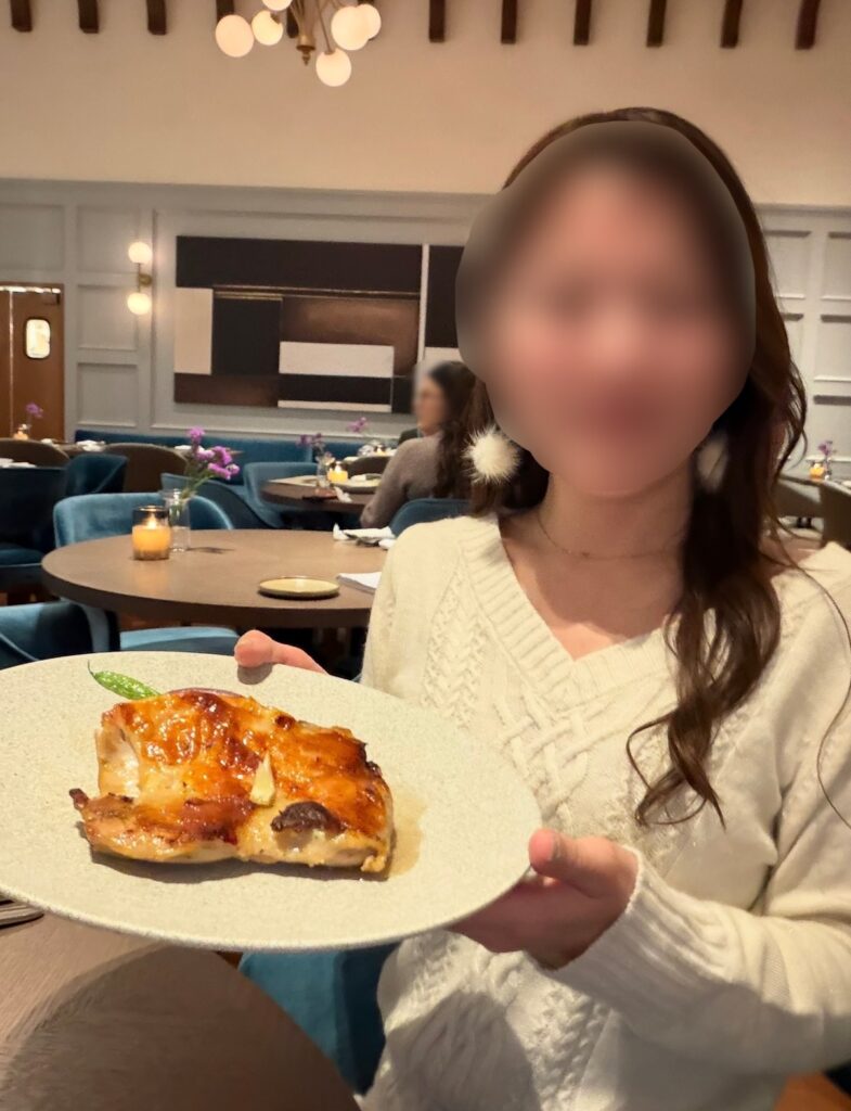 New American Dining GOTTAで提供されたメインディッシュ「さつま純然鶏のロースト」を手に持つブログ運営者COCO。ボリュームのあるチキン料理を前に、満足感のあるディナーの様子を伝える写真（※顔はぼかしを入れて掲載しています）。