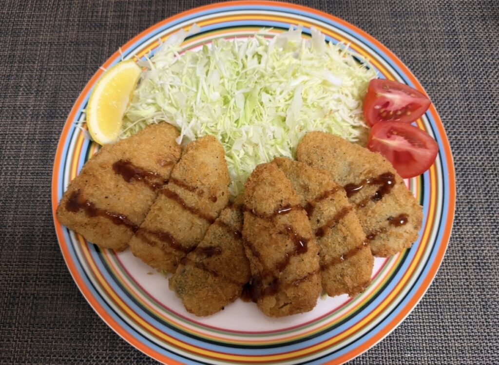 魚力95周年記念株主優待のアジフライを揚げて盛り付けた写真。千切りキャベツ、レモン、トマトを添えて実食した様子。