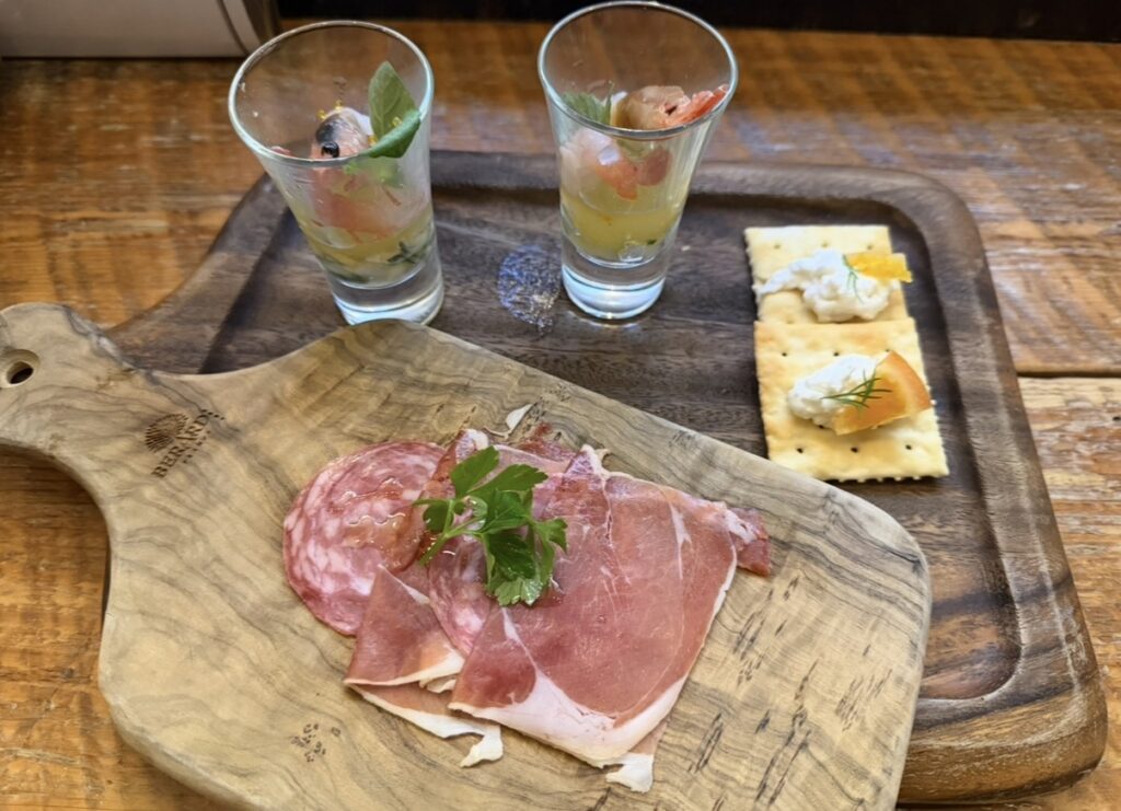 大崎キッチン（OSAKI KITCHEN）のデラックスコースのオードブル。シーフードカクテルの柚子胡椒ジュレ仕立て、スペイン産ハモンセラーノとサラミの盛り合わせ、ドライオレンジとカッテージチーズのブルスケッタが木製プレートに盛り付けられている。