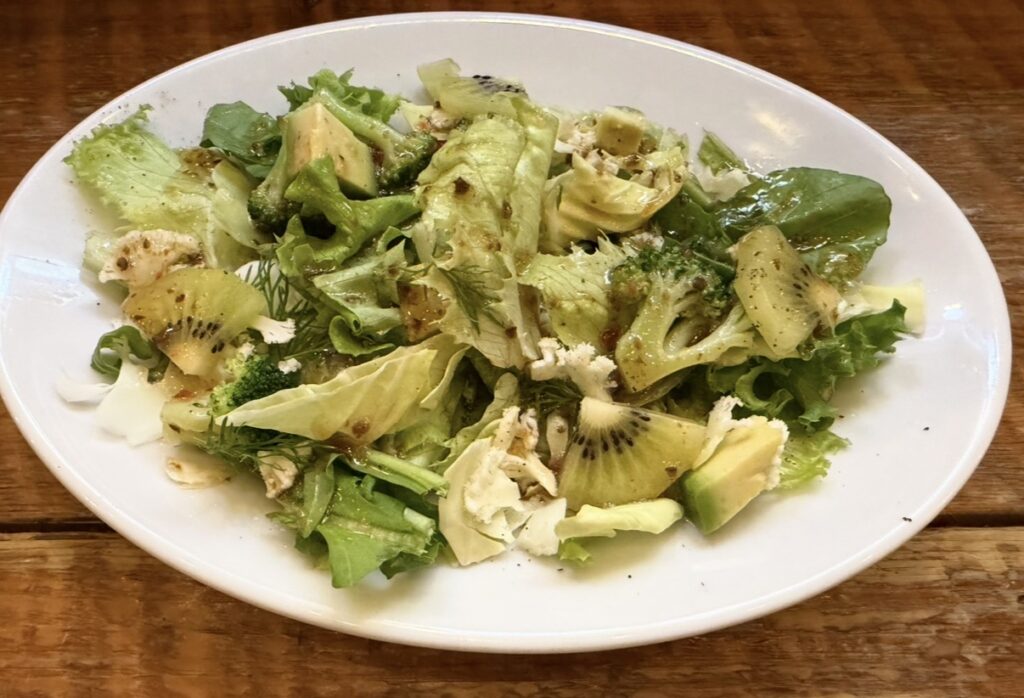 大崎キッチン（OSAKI KITCHEN）のデラックスコースで提供された「9種の野菜と果実のグリーンサラダ」。この日の果実はキウイで、アボカドやブロッコリー、リーフ野菜と一緒にさっぱりとしたドレッシングで仕上げられている。