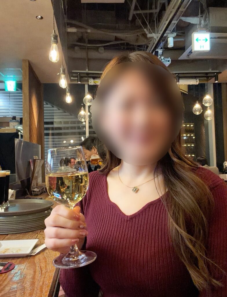 大崎キッチン（OSAKI KITCHEN）の店内で、白ワインを手に乾杯するブログ運営者COCO。飲み放題の白ワインをカルパッチョと合わせて楽しんでいる様子。※顔はぼかしを入れて掲載しています。