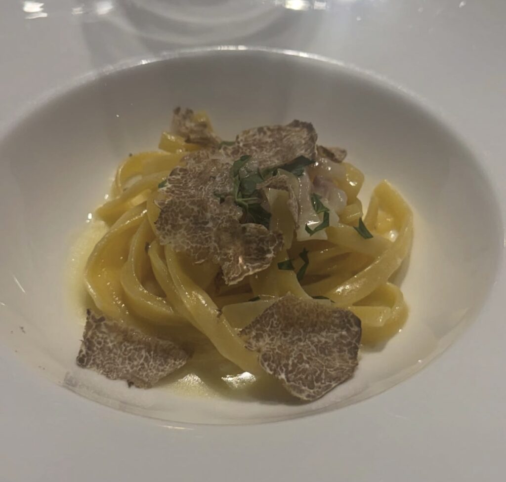 白トリュフの手打ちトレネッテ アマトリチャーナビアンコ。濃厚な白いソースにトリュフとパスタを盛り付けた一皿のアップ写真。
