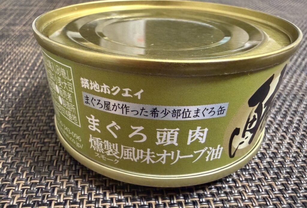 ゆうちょ銀行の株主優待で届いた築地魚河岸「希缶（まれかん）」シリーズの
まぐろ頭肉スモーク風味オリーブ油の缶詰写真。
ゴールドの缶に「築地ホクエイ」「希缶」と書かれ、上品で高級感のあるデザイン。
燻製の香ばしさとオリーブオイルのまろやかさが特徴の一品。