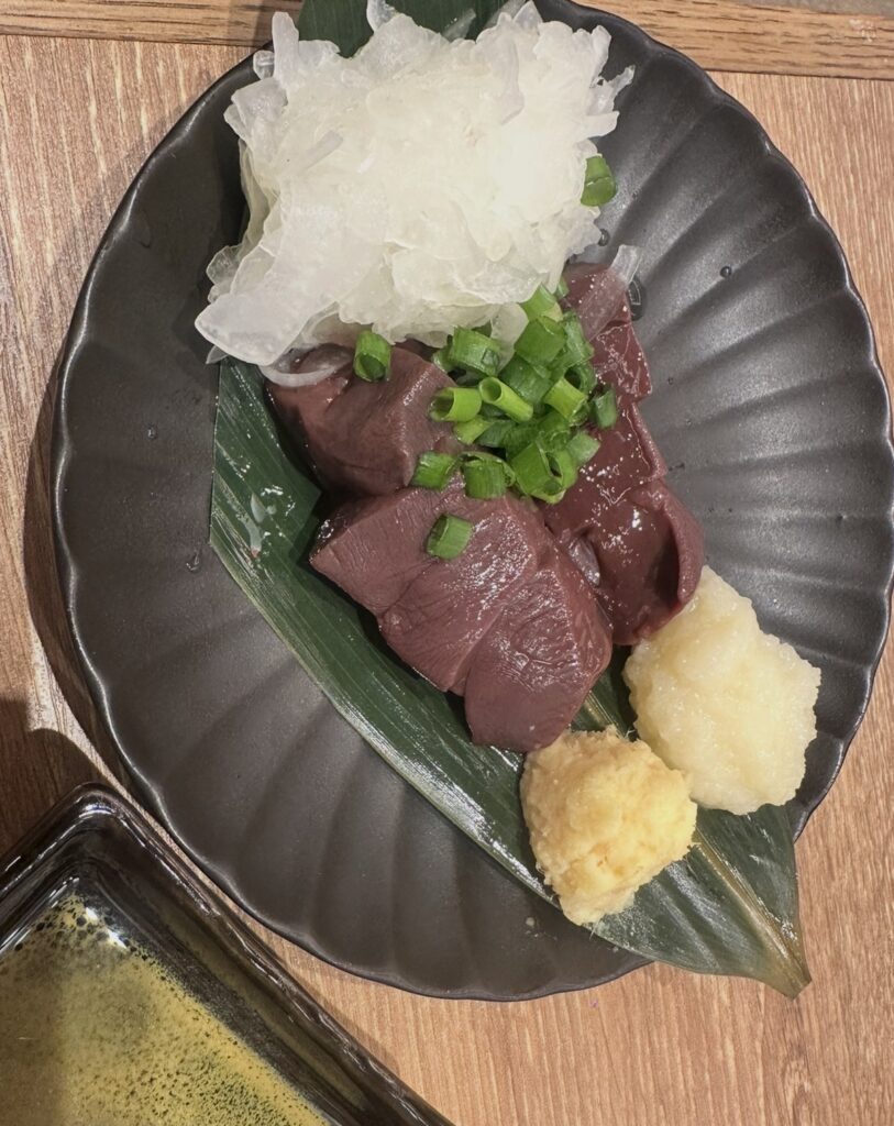 ダンダダンの『馬レバー』の一皿。黒い丸皿の上に新鮮な馬レバーが切り身で盛りつけられ、玉ねぎスライス・生姜・にんにくが添えられている。葉の上に美しく並べられた色艶のあるレバーが印象的な写真。