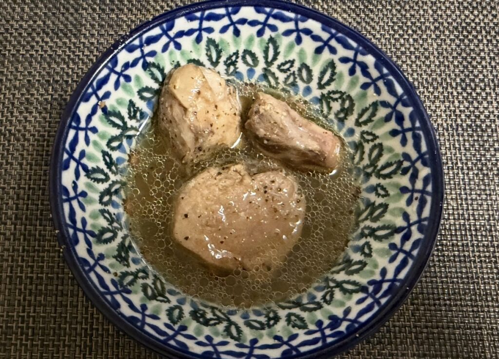 ゆうちょ銀行の株主優待で届いた築地魚河岸「希缶」シリーズ、まぐろ尾肉・黒胡椒オリーブ油の中身。大きめの尾肉が3切れ入っており、黒胡椒が効いたオリーブオイルに浸された贅沢な煮込み。和柄の深皿に盛り付けた様子を上から撮影した写真。
