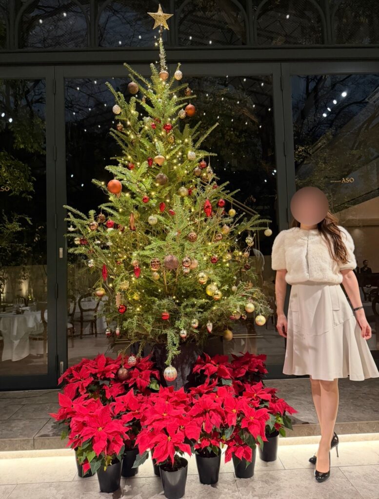 リストランテASOの店内に飾られた大きなクリスマスツリーの前で撮影した、ブログ運営者COCOの写真。クリスマスの予約初日に申し込んだことで、ツリーの目の前の席に案内され、特別な雰囲気の中でディナーを楽しんだ様子。※顔はぼかしを入れて掲載しています。