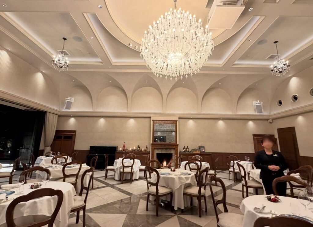 リストランテASOのメインダイニングの様子。天井に輝くシャンデリアと、ゆったり配置されたテーブルが並ぶクラシックで上品な空間が、特別なディナーの雰囲気を演出している。