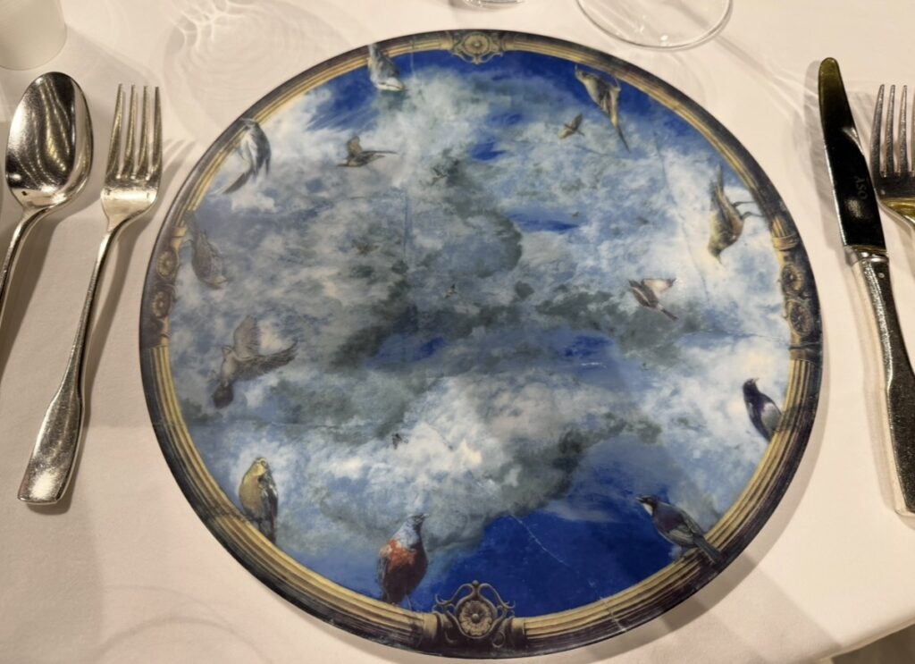 リストランテASOのテーブルに置かれた、天井画「碧空」と同じモチーフのデザイン皿。青空と鳥が描かれたプレートが、これから始まるクリスマスディナーへの期待を高めてくれる。