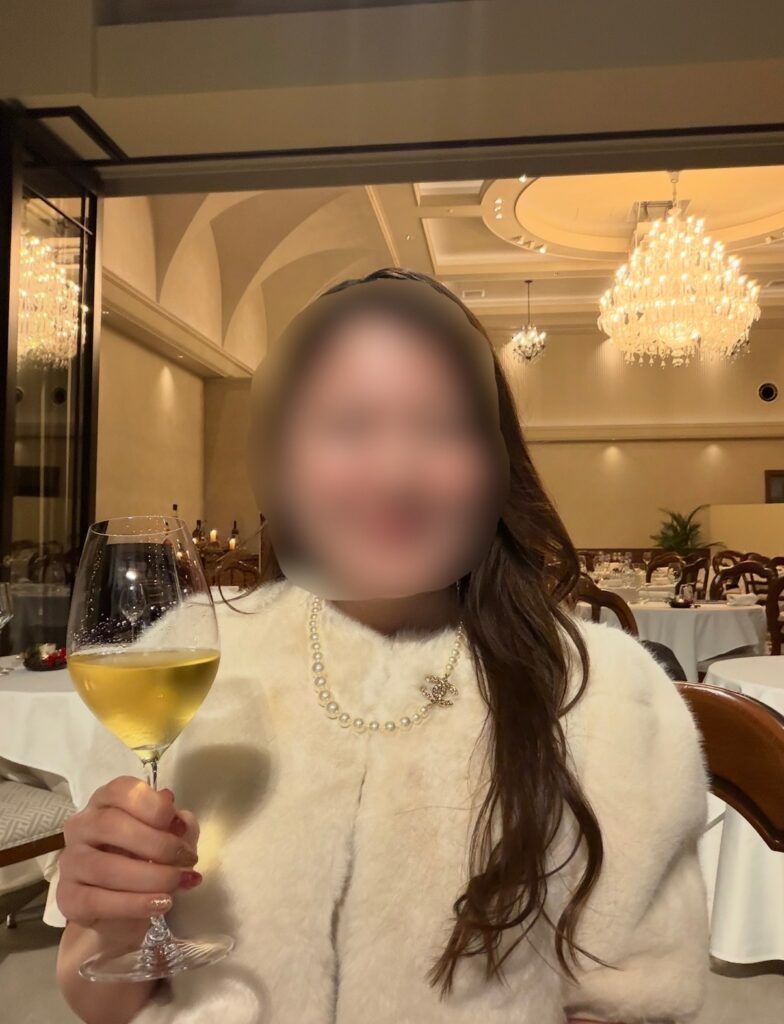 リストランテASOのクリスマスディナーで、ワインペアリングの1杯目を手にするブログ運営者COCO。シャンデリアが輝く店内で、特別な夜のひとときを楽しんでいる様子。※顔はぼかしを入れて掲載しています