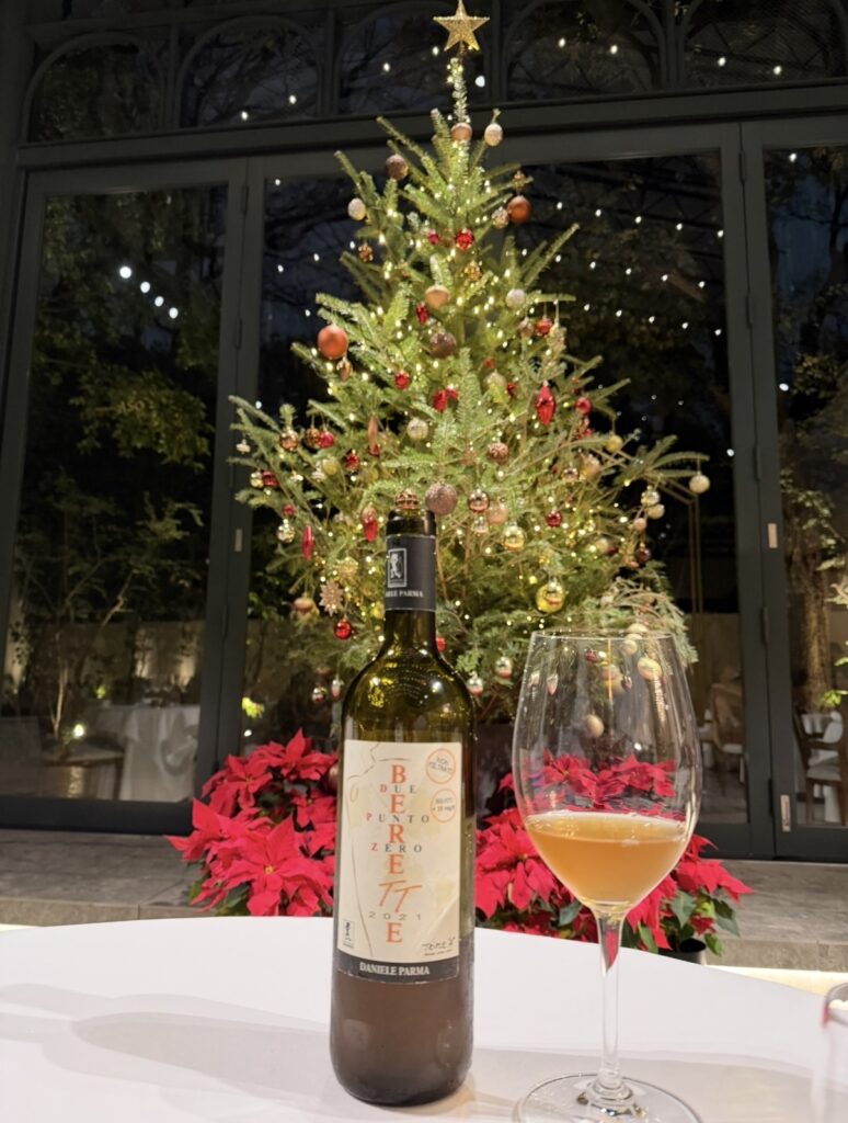 クリスマスディナーのペアリング3杯目として提供されたワイン「ベーレ・プント・ゼロ TT 2021（ダニエレ・パルマ）」。クリスマスツリーを背景に、ワインボトルとグラスを並べた一枚。
