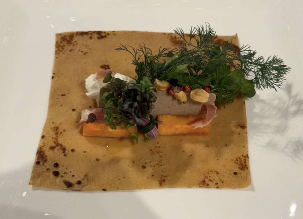 クリスマスディナーの前菜「白レバーと柿のサラダ ネッチ風」。クレープ状の生地の上に白レバーやハーブ、フルーツを盛り付けた華やかな一皿。
