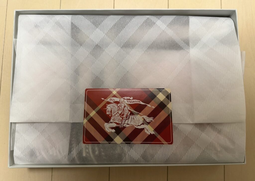 バーバリーで購入したチェックカシミアスカーフのギフトボックス。包み紙の上に、限定紙袋と同じチェック柄デザインのシールが貼られている様子。