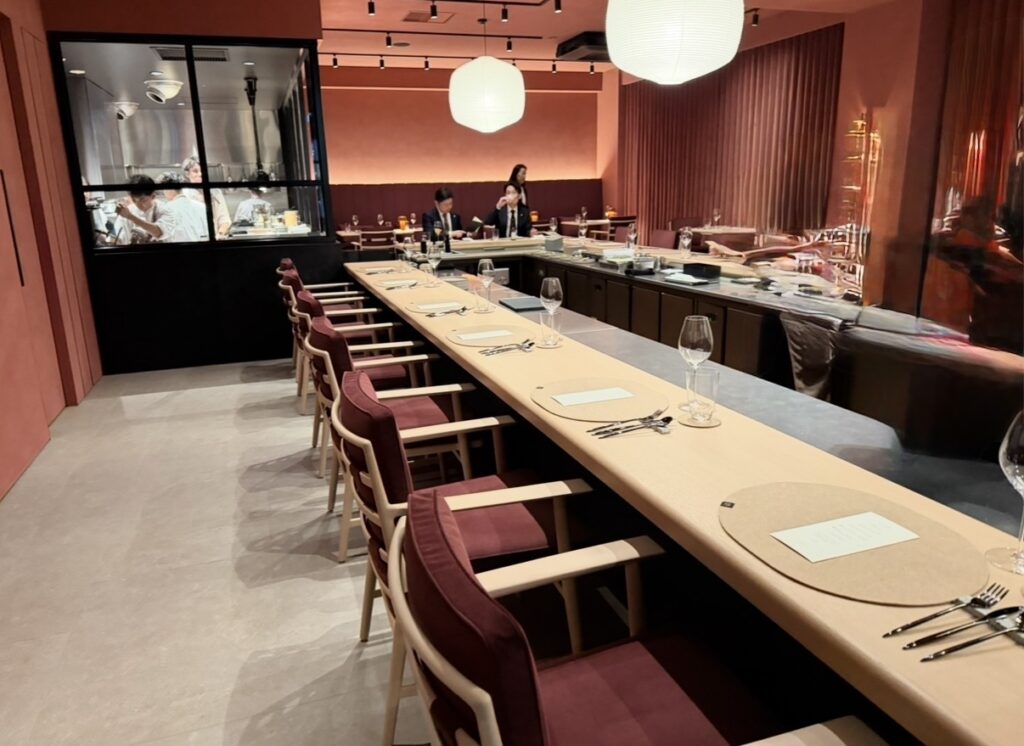 ひらまつ新店舗「HRMT STAGE」の店内の様子。オープンキッチンを囲むカウンター席が並び、落ち着いた色合いの空間で食事を楽しめるレストランの雰囲気。