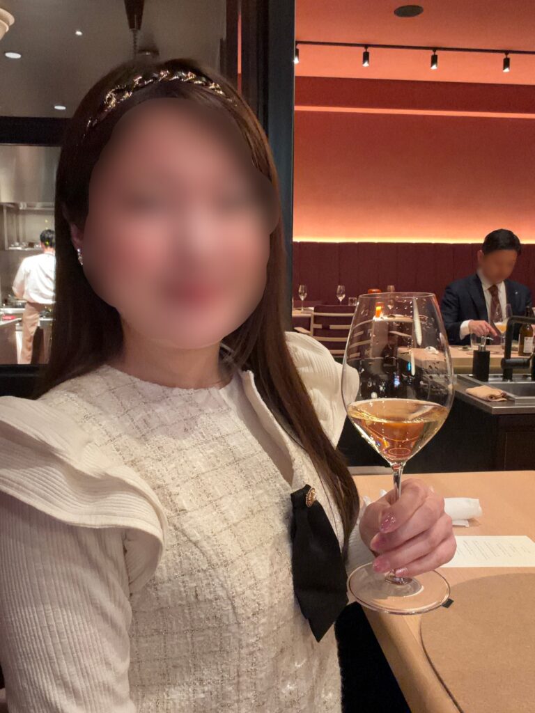 ひらまつ新店舗「HRMT STAGE」のカウンター席で、ワインペアリング1杯目のシャンパンを楽しむ様子。※顔はぼかしを入れて掲載しています。