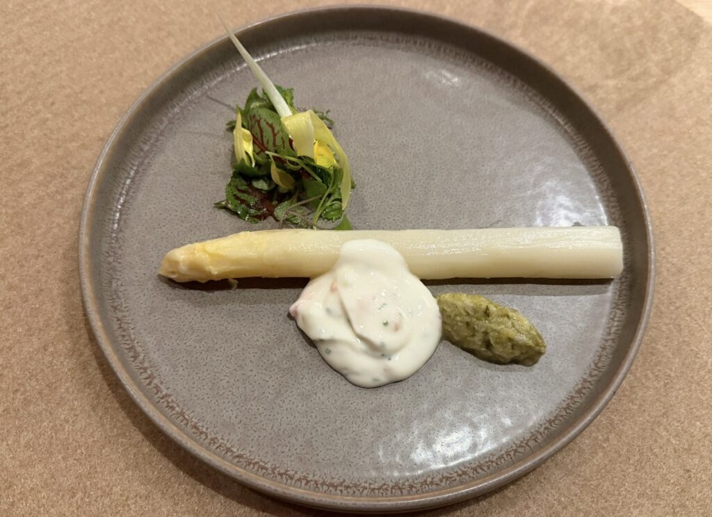 ひらまつ新店舗「HRMT STAGE」のコース前菜、ホワイトアスパラガスとフキの芽。太くみずみずしいホワイトアスパラにクリーミーなソースとフキの芽のペーストが添えられた一皿。