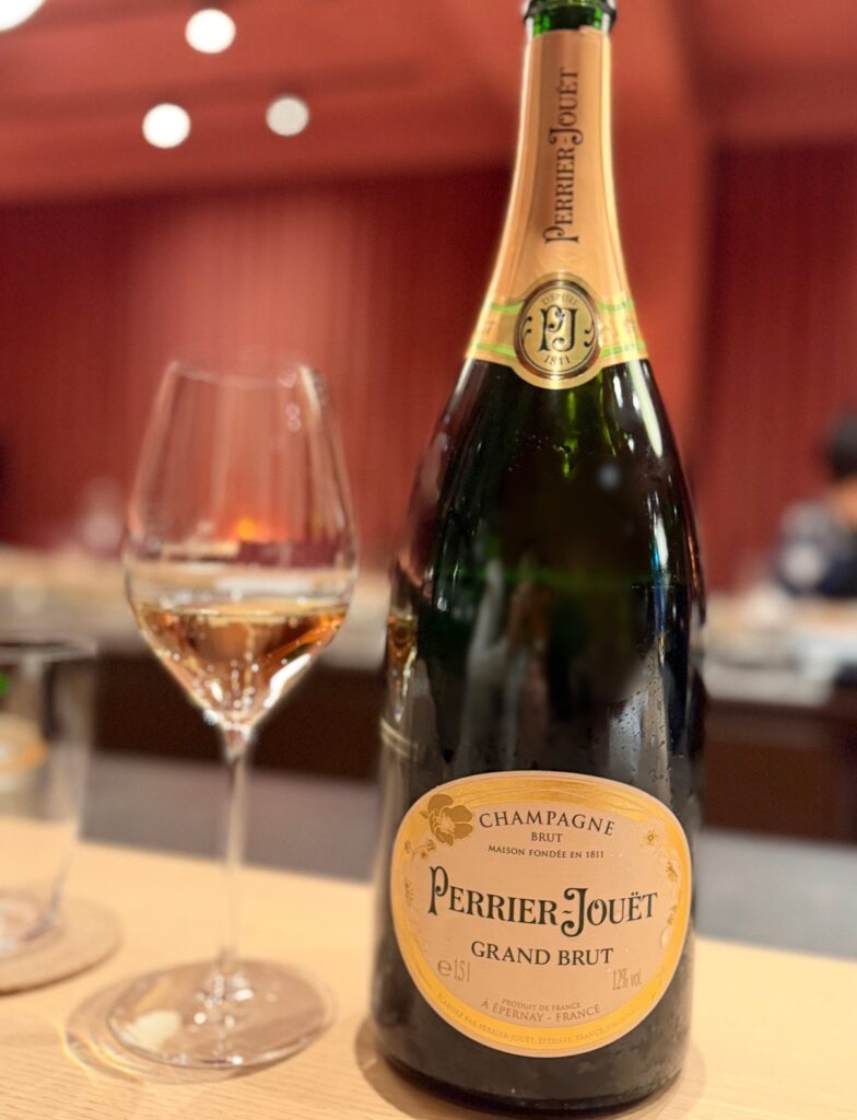 ひらまつ新店舗「HRMT STAGE」のワインペアリング1杯目として提供されたシャンパン「ペリエ・ジュエ グラン・ブリュ」。グラスに注がれたシャンパンとボトルの写真。