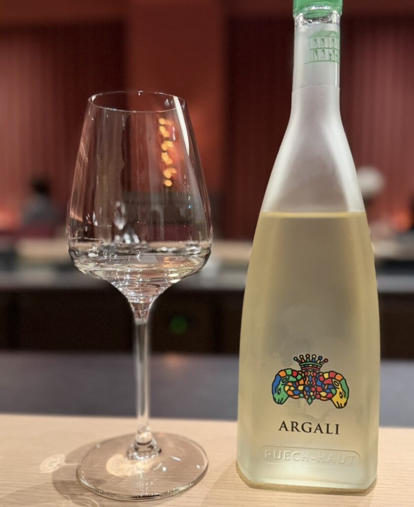 ひらまつ新店舗「HRMT STAGE」のワインペアリング3杯目として提供された白ワイン「アルガリ(Puech-Haut)」。グラスに注がれた白ワインとボトルの写真。
