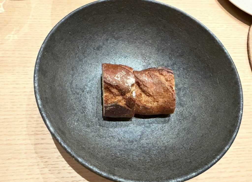 ひらまつ新店舗「HRMT STAGE」で提供された自家製パンドカンパーニュ。香ばしく焼き上げられたパンが黒いプレートに盛り付けられている様子。