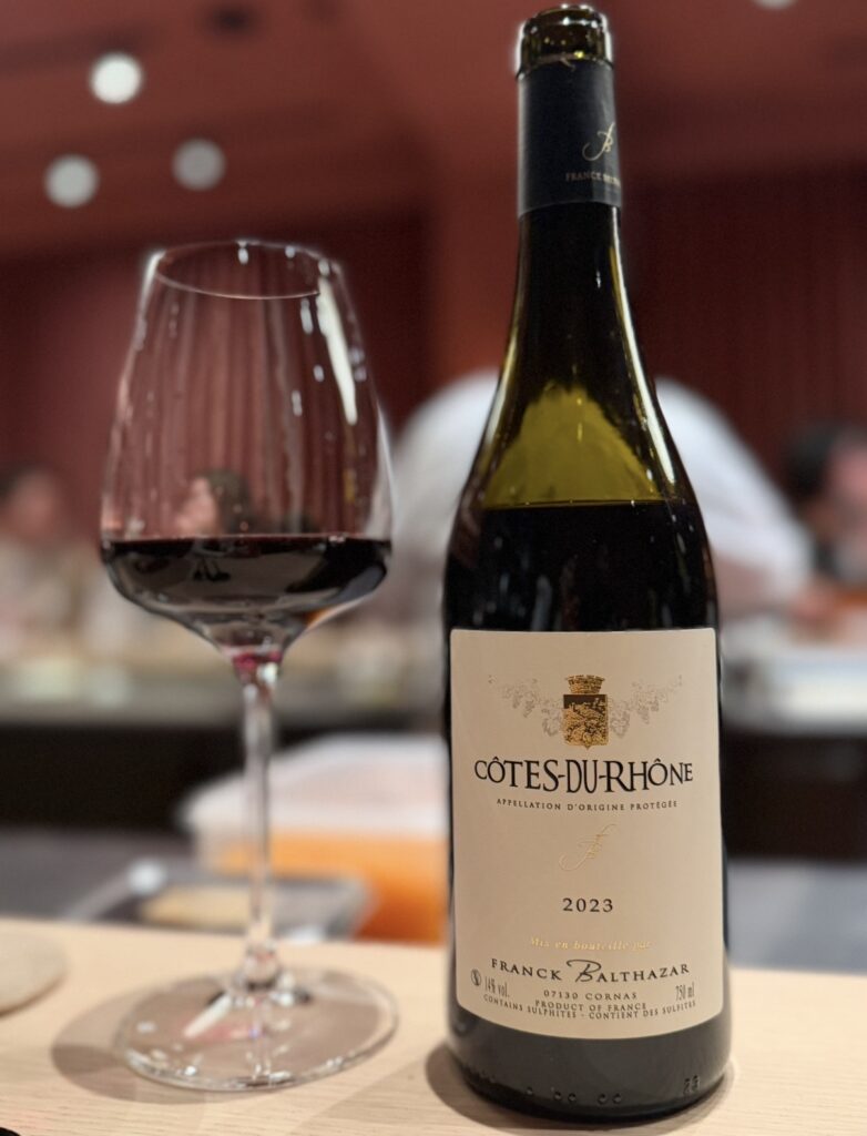 ひらまつ新店舗「HRMT STAGE」で追加注文した赤ワイン、コート・デュ・ローヌ(フランク・バルタザール)2023。グラスに注がれた赤ワインとボトルの写真。