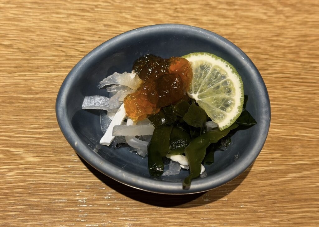 北の味紀行と地酒 北海道の限定小鉢「とらふぐ皮 柚子ポンジュレ」。とらふぐの皮にわかめと柚子の輪切り、柚子ポン酢ジュレがのった前菜