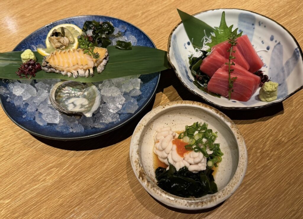 北の味紀行と地酒 北海道で注文した海鮮料理の盛り合わせ。活蝦夷アワビ刺身、まぐろの赤身の刺身、白子ポン酢がテーブルに並んでいる様子