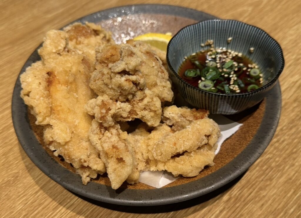 北の味紀行と地酒 北海道で注文したたれざんぎ。甘辛いタレに絡めた鶏の唐揚げが皿に盛られ、タレ用の小鉢が添えられている。