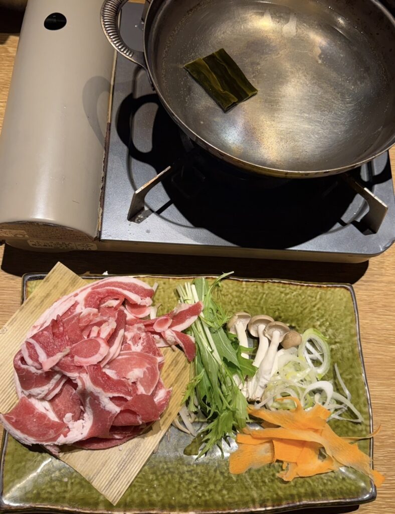 北の味紀行と地酒 北海道で注文したラムしゃぶしゃぶのセット。薄切りのラム肉と野菜が盛り付けられ、卓上コンロの鍋でしゃぶしゃぶする様子