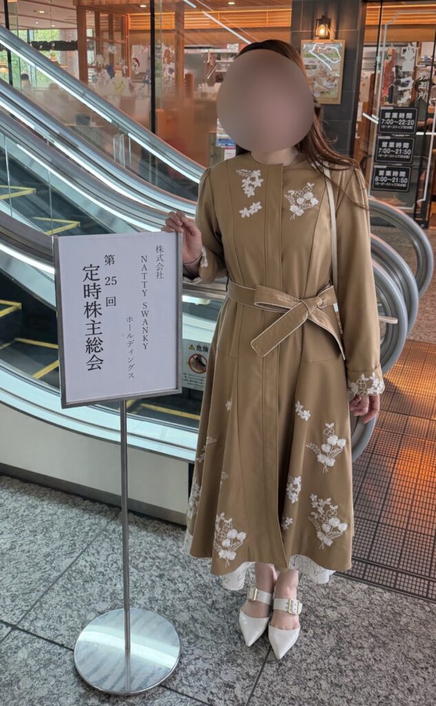 ナッティースワンキー（7674）株主総会の案内看板の前で撮影したブログ運営者COCO（※顔はぼかしを入れて掲載しています）