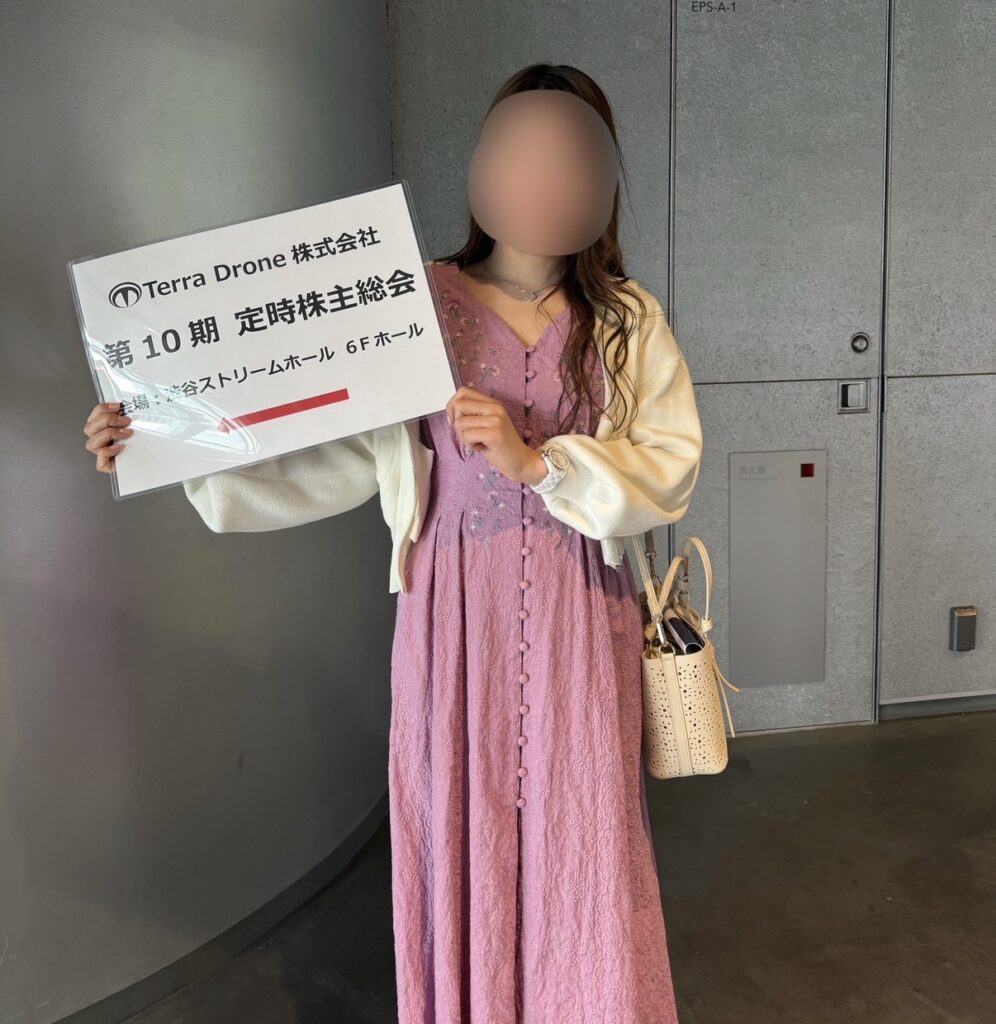 テラドローン第10期定時株主総会の会場前で、案内パネルを持って撮影したブログ運営者COCOの写真（※顔はぼかしを入れて掲載しています）