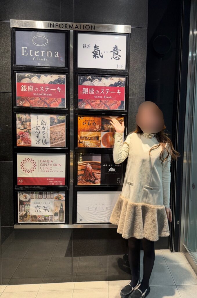 グランベル銀座ビルⅡの館内案内板の前で立つブログ運営者COCO。銀座のステーキの看板が8階と9階に表示されており、同じビル内に複数の飲食店が入っている様子 ※顔はぼかしを入れて掲載しています