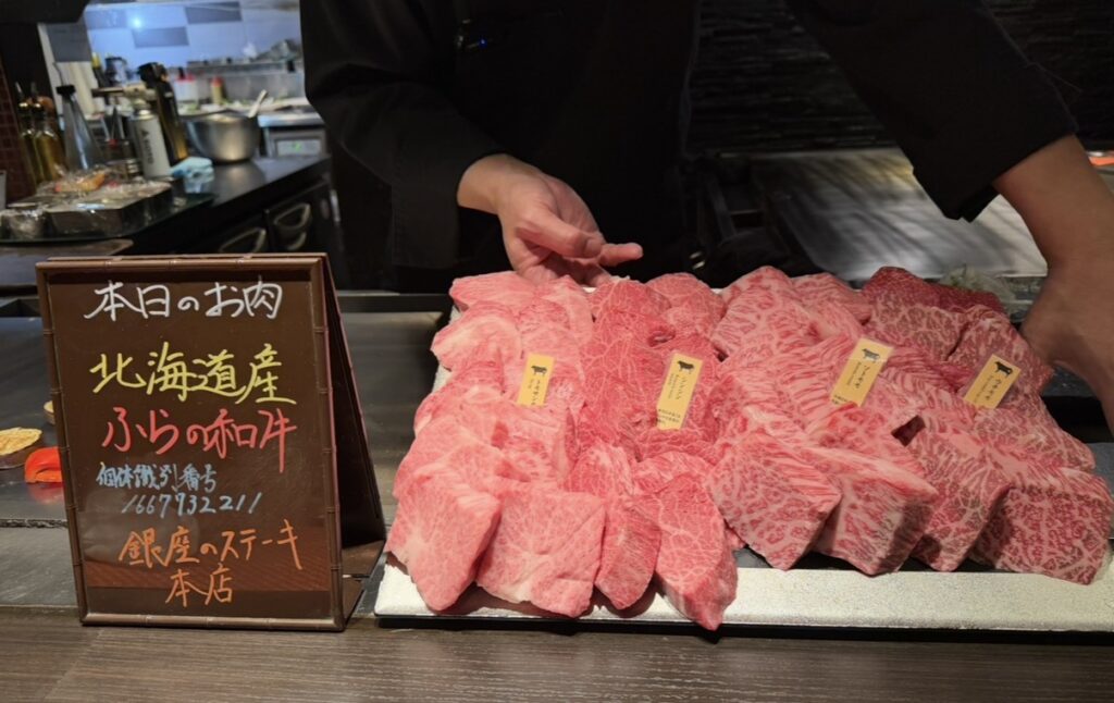 銀座のステーキ銀座本店で提供される本日のA5黒毛和牛の産地と個体識別番号が表示された案内と、複数の部位が並べられた様子。北海道産ふらの和牛と記載されている