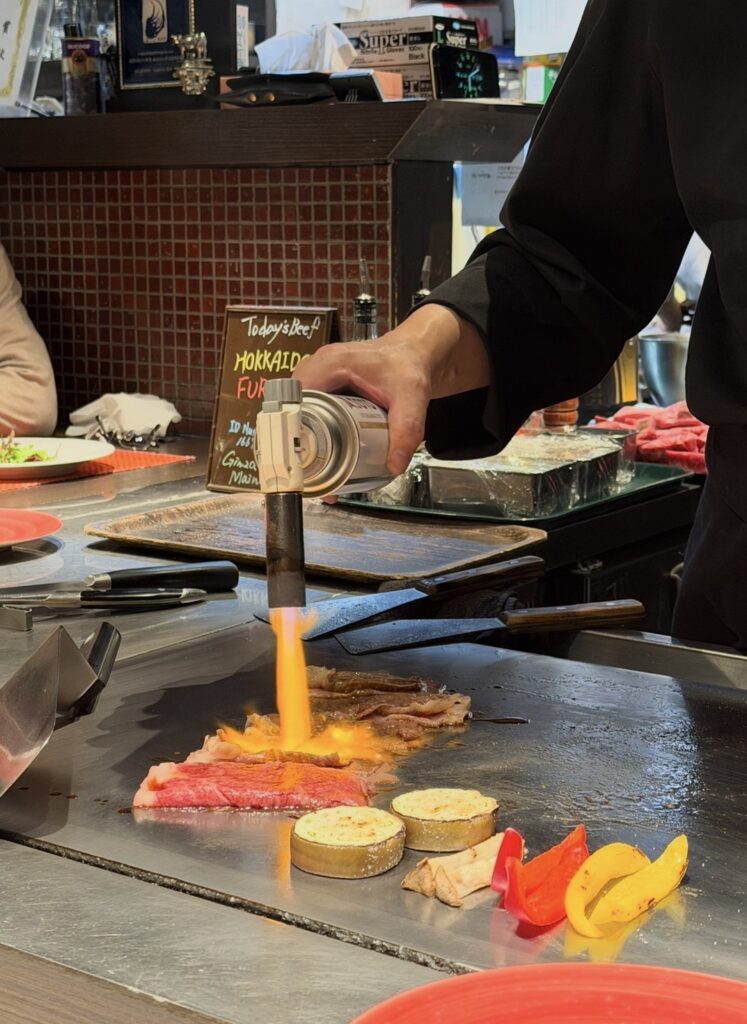 銀座のステーキ銀座本店でA5黒毛和牛を鉄板の上でバーナーを使って焼き上げている様子。炎を使った調理で香ばしさを引き出している
