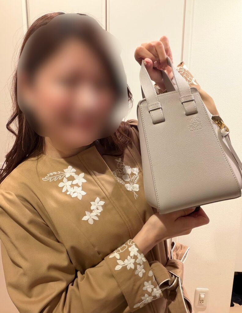 ブログ運営者COCOがロエベのハンモックバッグ コンパクト（ライトゴースト）を手に持っている様子。上品なベージュ系コーデとバッグカラーがマッチしている ※顔はぼかしを入れて掲載しています。