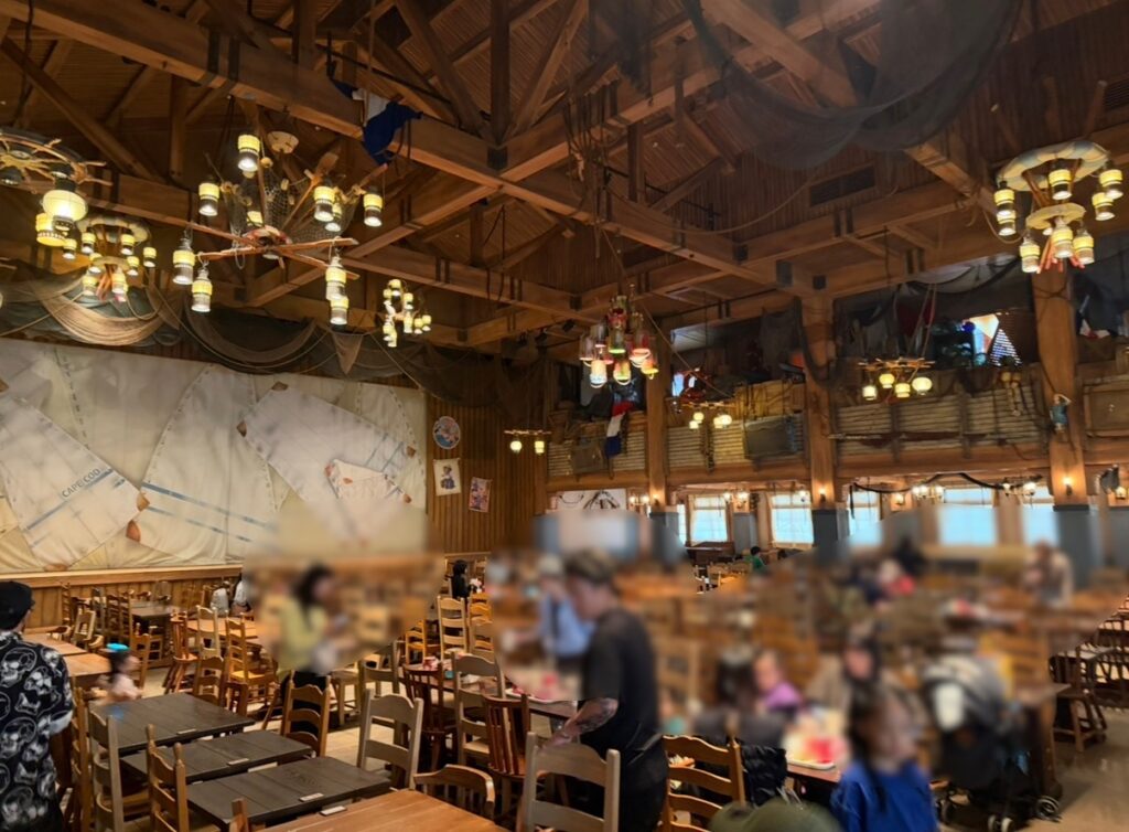 東京ディズニーシー「ケープコッド・クックオフ(ショーダイニングエリア)」の店内の様子。木の温もりあふれる広々とした空間に、たくさんのテーブル席が並んでいる。