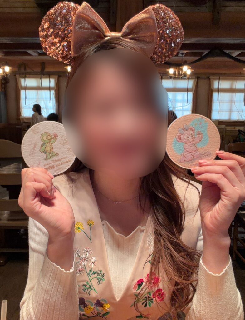 ブログ運営者COCOが東京ディズニーシー「ダッフィー&フレンズのワンダフル・フレンドシップ」のスーベニアコースターを手に持って記念撮影している様子。シェリーメイとオル・メルのコースターを披露している写真。