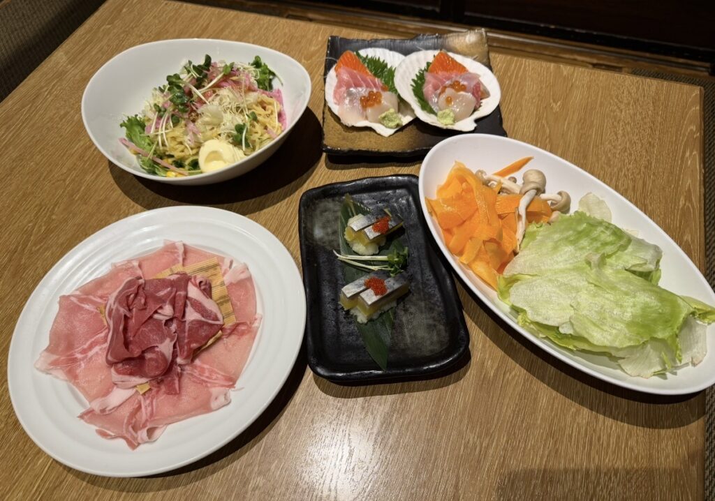 「北の味紀行と地酒 北海道の北海道コースで提供された前菜や刺身、しゃぶしゃぶ用の豚肉とラム肉」の写真。